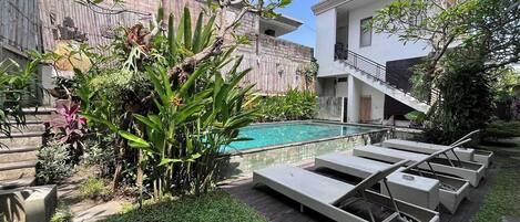 A poolside area with lounge chairs, a wooden deck, and a variety of plants.