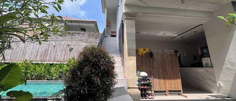 A residential building with a swimming pool, a covered outdoor area, and a staircase leading to the upper floor.