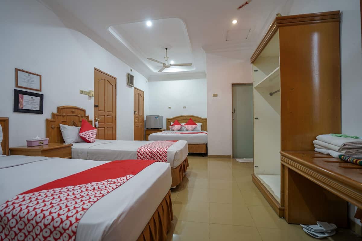 Habitación de hotel con tres camas, ventilador de techo, armario de madera y un espejo.