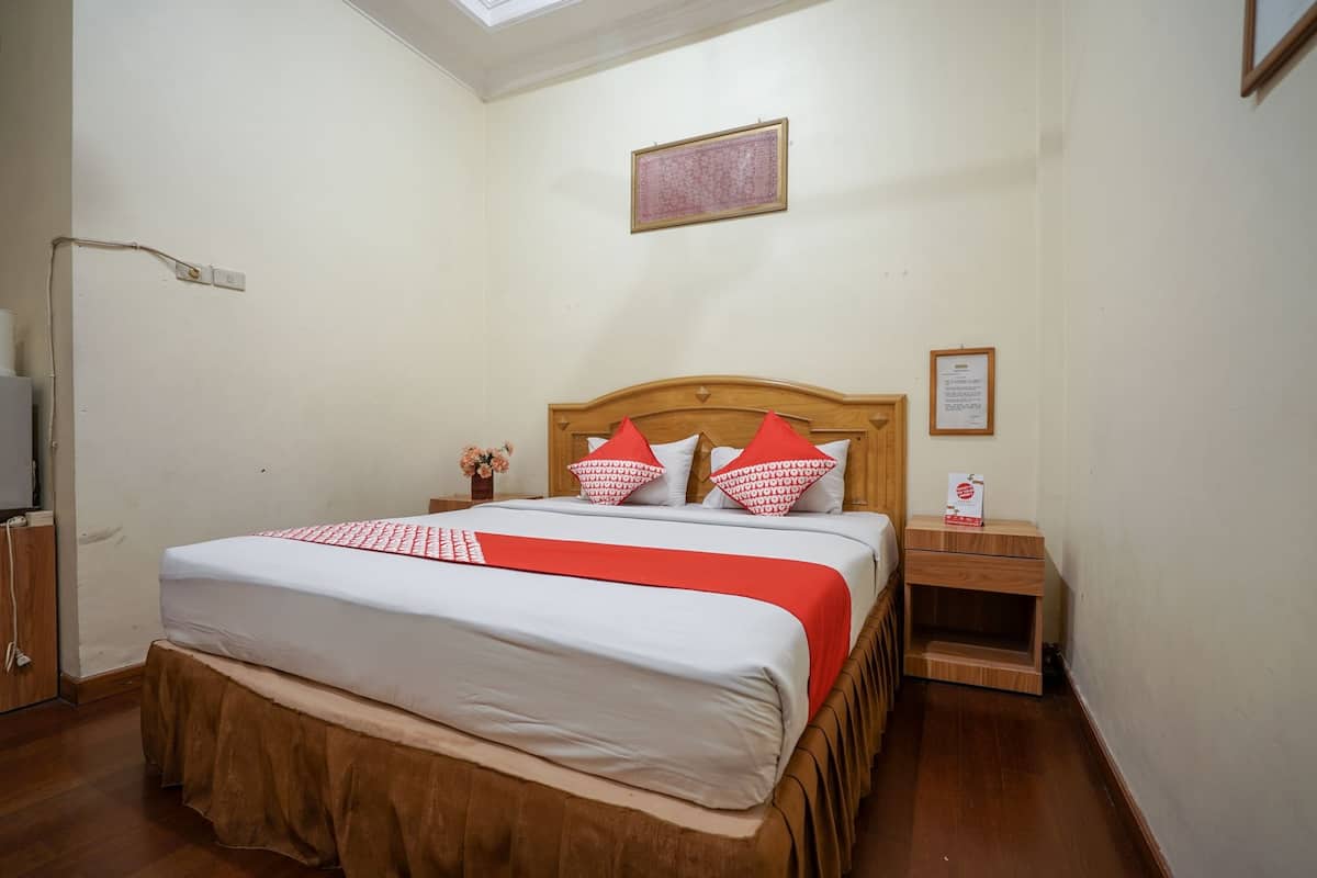 Un dormitorio ordenado con una cama de madera, una mesita de noche y una pequeña lámpara de noche, además de un cuadro en la pared.