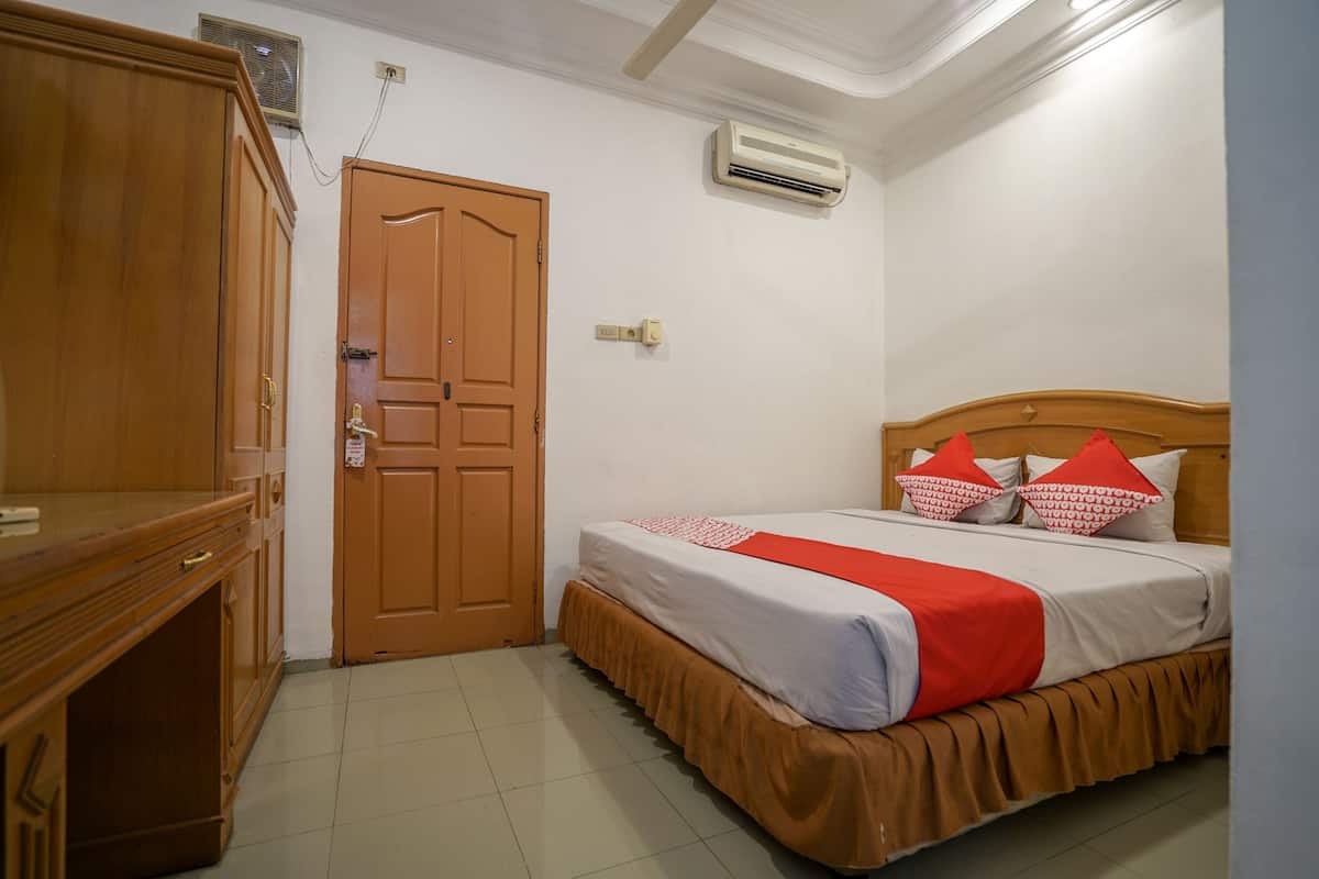 Un dormitorio con un armario de madera, una cama con colcha roja y blanca, y un equipo de aire acondicionado en la pared.