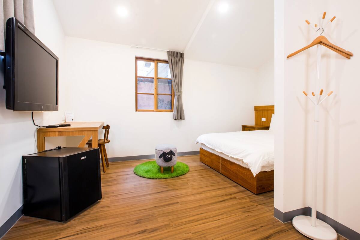 Une chambre d’hôtel comprenant un lit, un bureau, une télévision, une armoire et un tapis vert orné d’un motif de mouton.