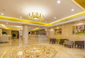 Un vestíbulo de hotel con una gran lámpara de araña, un mostrador de recepción y una alfombra decorativa de gran tamaño.
