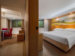 Una habitación de hotel con una cama, un escritorio con una silla, un cuadro en la pared y vistas a árboles por la ventana.