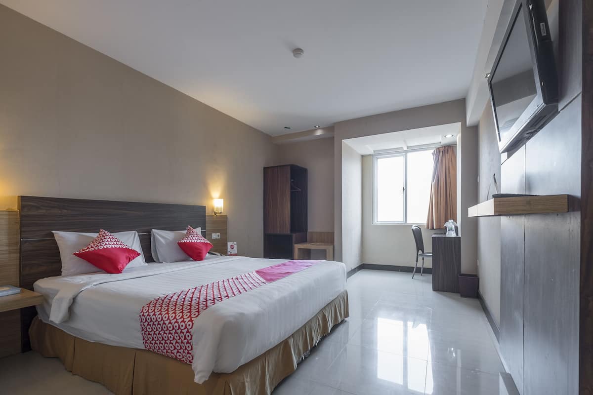 Une chambre d’hôtel avec un grand lit, un téléviseur fixé au mur, un bureau et une fenêtre avec des rideaux.