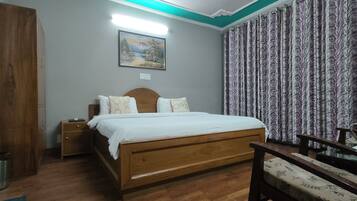 Un dormitorio con cama de madera, mesita de noche, una silla, un cuadro en la pared y cortinas.