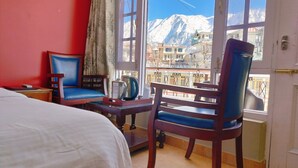 Habitación de hotel con cama, dos sillas azules, una mesita con tetera y vistas a montañas nevadas.