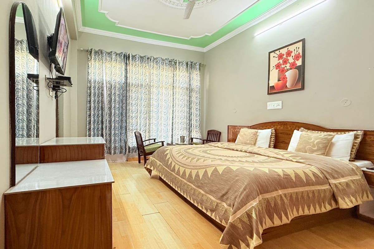 Une chambre à coucher avec un lit, un bureau, une chaise, un miroir et une fenêtre avec des rideaux.