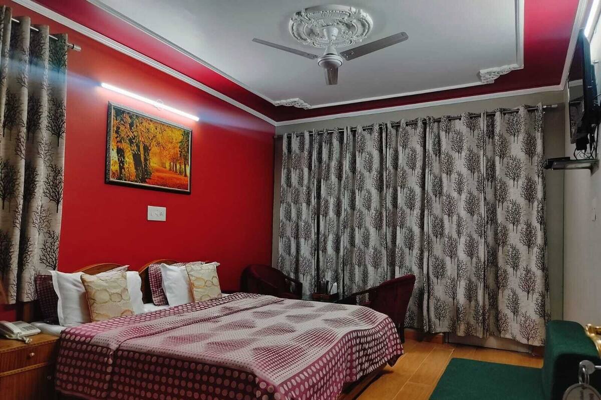 Une chambre à coucher comprenant un lit, une table de chevet, un bureau, une chaise, un banc vert, un ventilateur de plafond et un tableau accroché au mur.