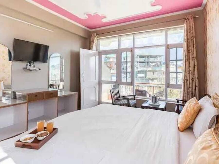 A hotel room with a bed, a desk, a TV, and a window with a view of buildings.
