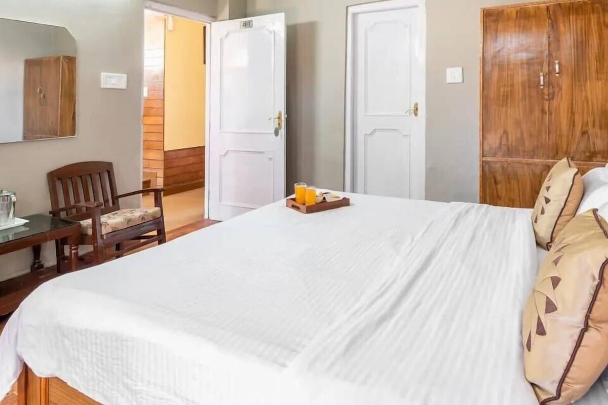 Une chambre d’hôtel avec un grand lit, une armoire en bois, un bureau avec une chaise et un miroir au mur.