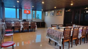Un comedor con mesas y sillas de madera, un ventanal con vistas y un televisor montado en la pared.