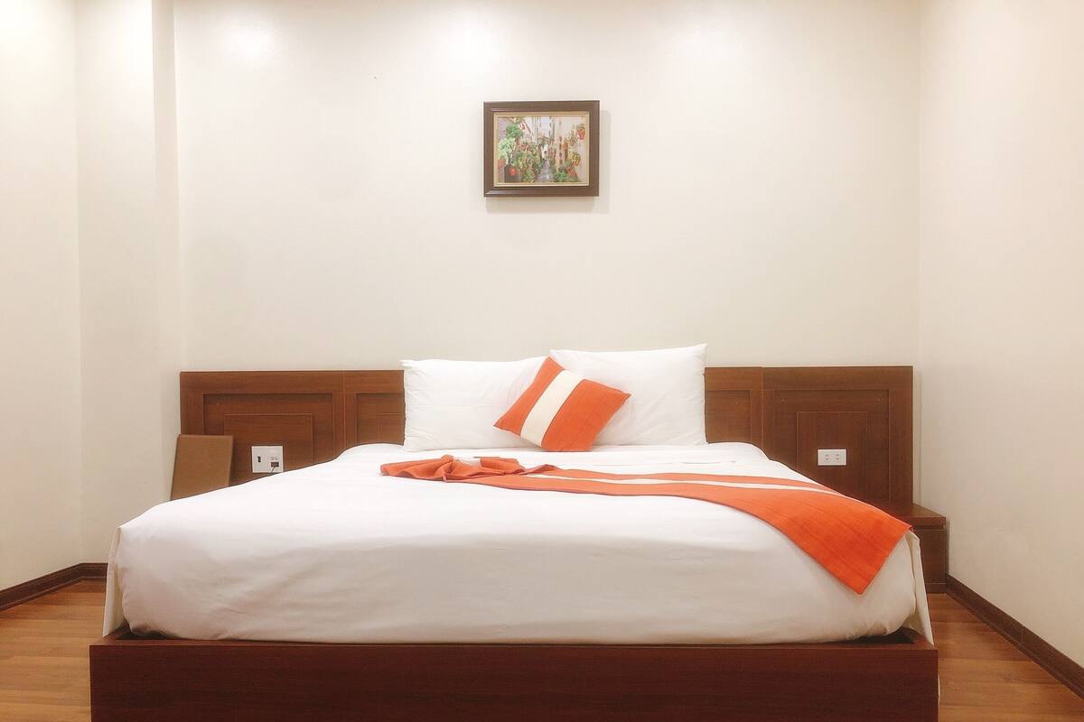 A neatly made bed with white and orange bedding, a wooden headboard, and a small framed picture on the wall.