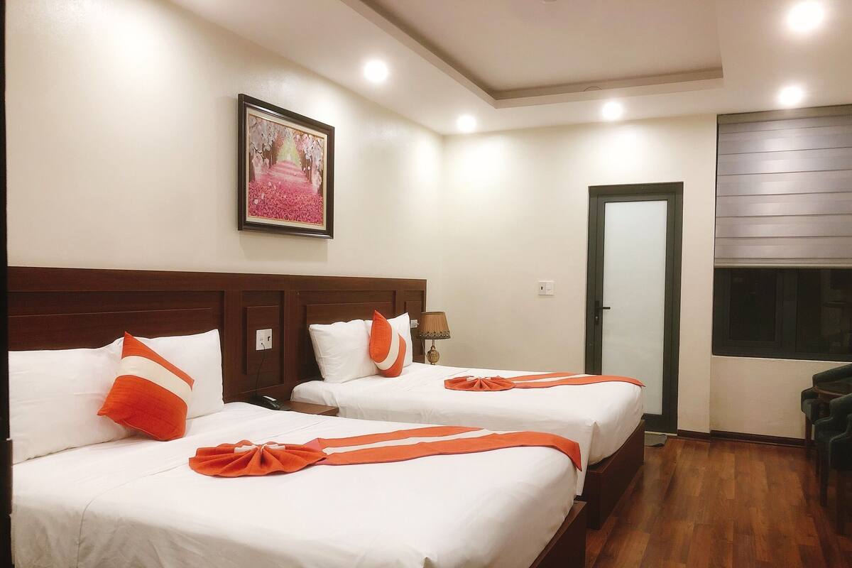 A hotel room with two beds, wooden headboards, white bedding, and an orange decorative ribbon.
