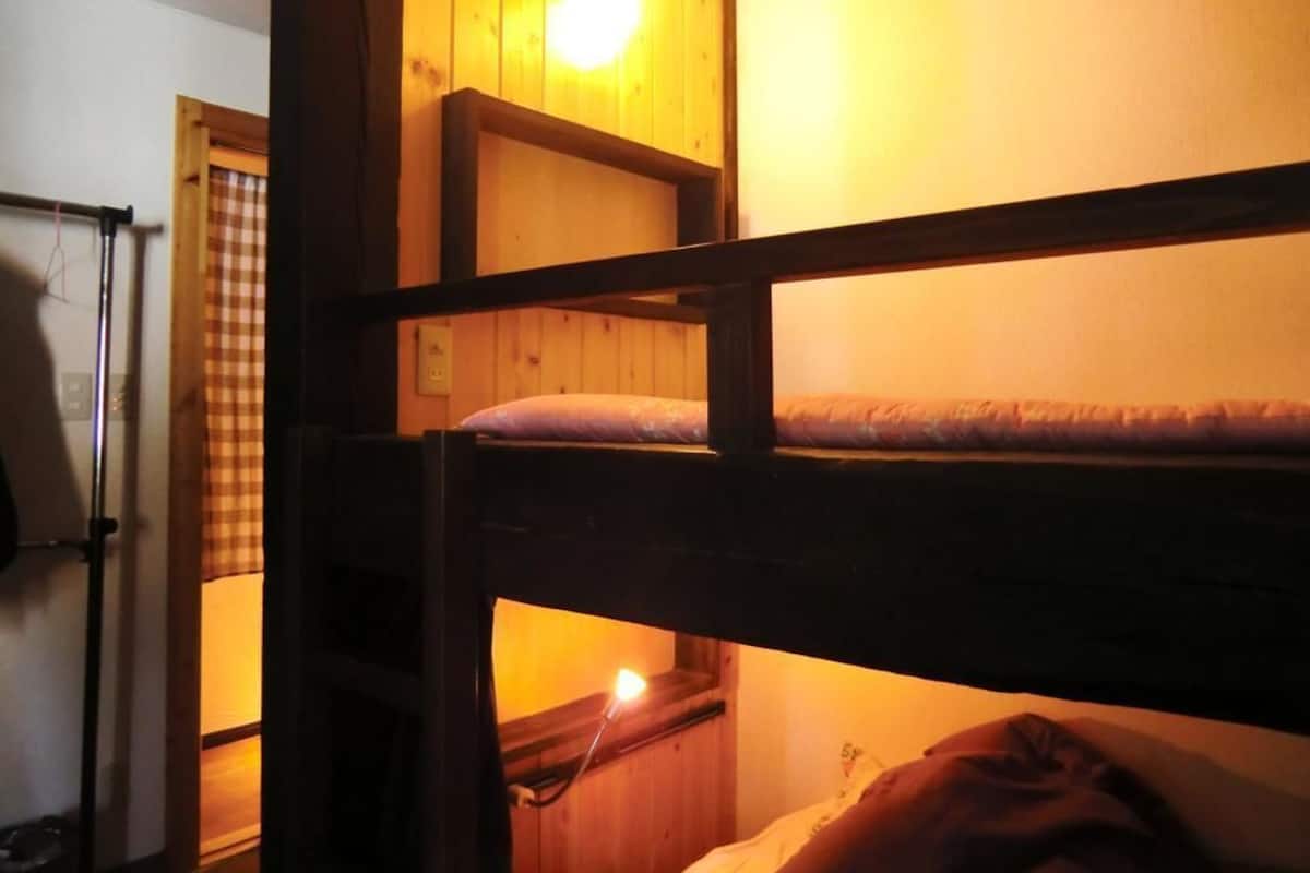Habitación con literas, paredes de madera y una única fuente de luz.