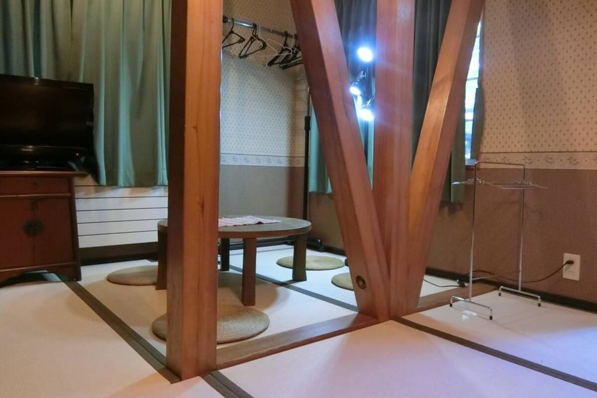 Una habitación con tatamis, un televisor, una mesita redonda y un perchero.