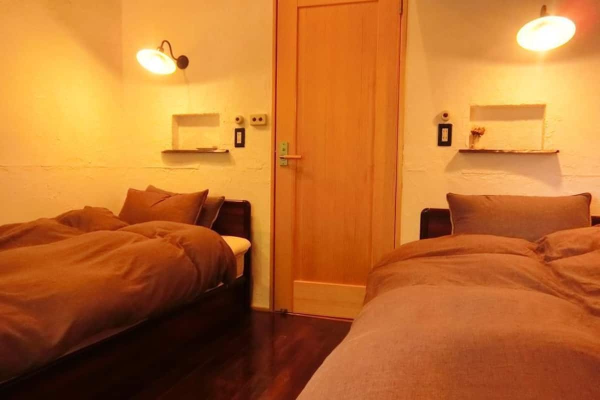 Una habitación con dos camas, una puerta de madera y luces fijadas a la pared.