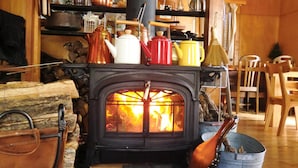 Una habitación acogedora con una estufa de leña, un comedor con sillas de madera y varios utensilios de cocina en estantes.