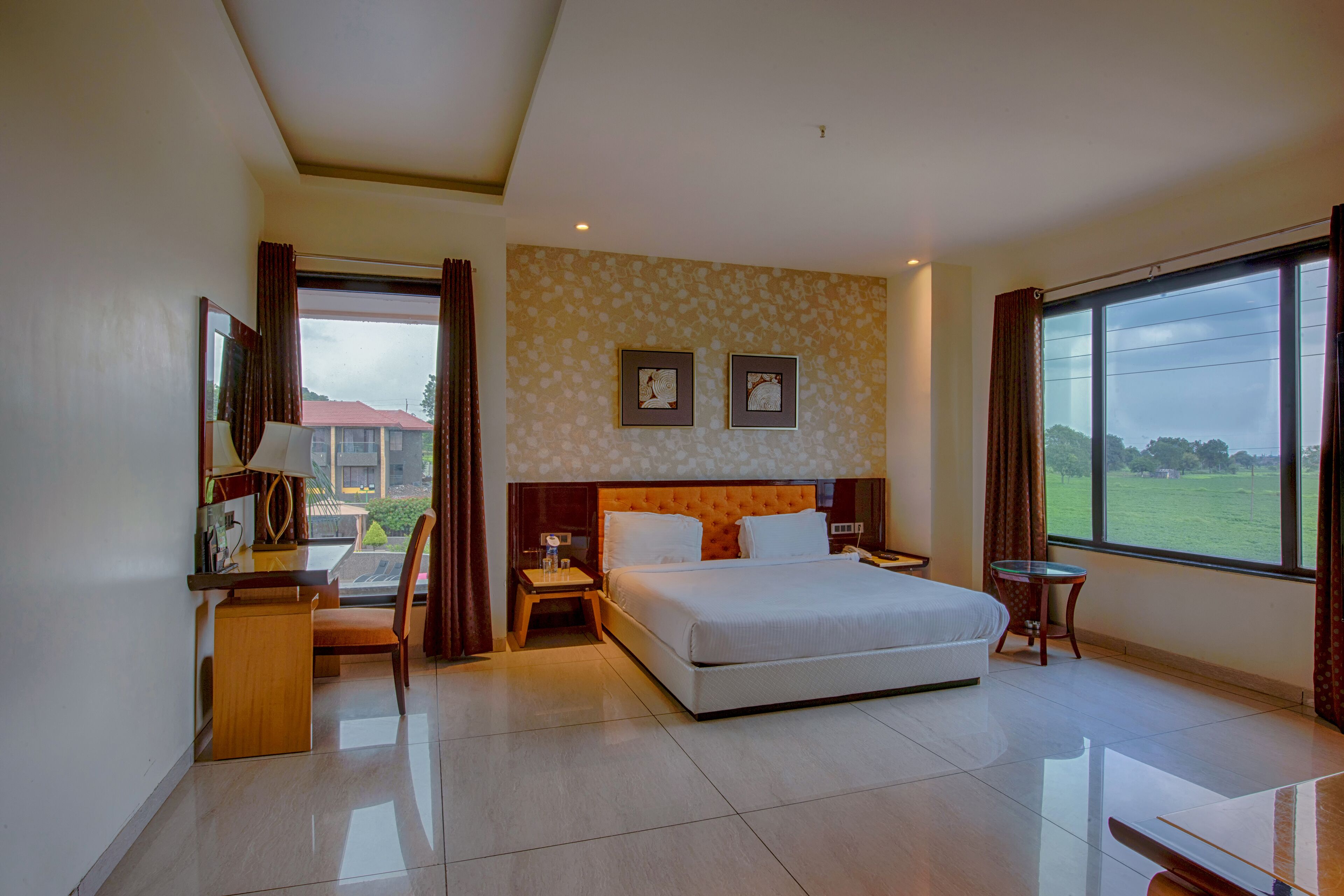 A hotel room with a bed, a desk, a chair, a small table, and a window with a view of the outdoors.