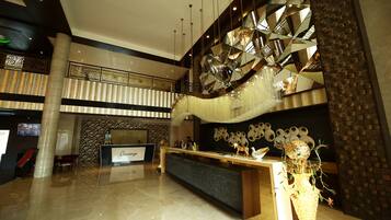 A spacious lobby with a reception desk, a decorative wall, and a large chandelier.