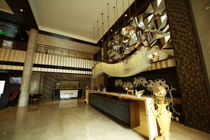 A spacious lobby with a reception desk, a decorative wall, and a large chandelier.