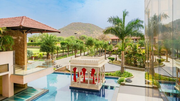 A resort pool area with a gazebo, palm trees, and a mountain in the background. - Crescent Spa And Resorts Indore (Indore)