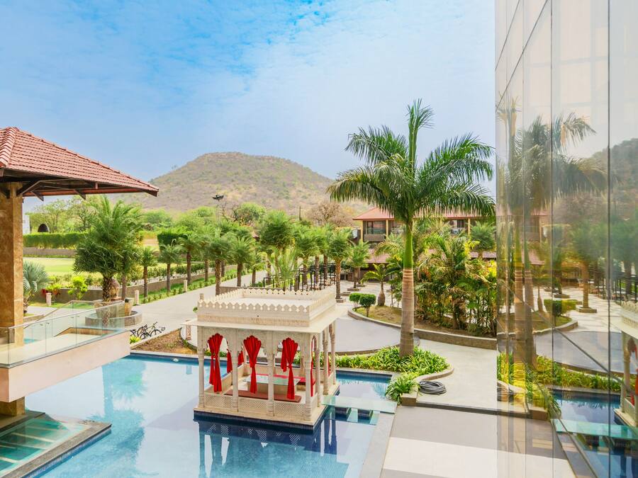 Zona de piscina de un resort con un pabellón, palmeras y una montaña al fondo.