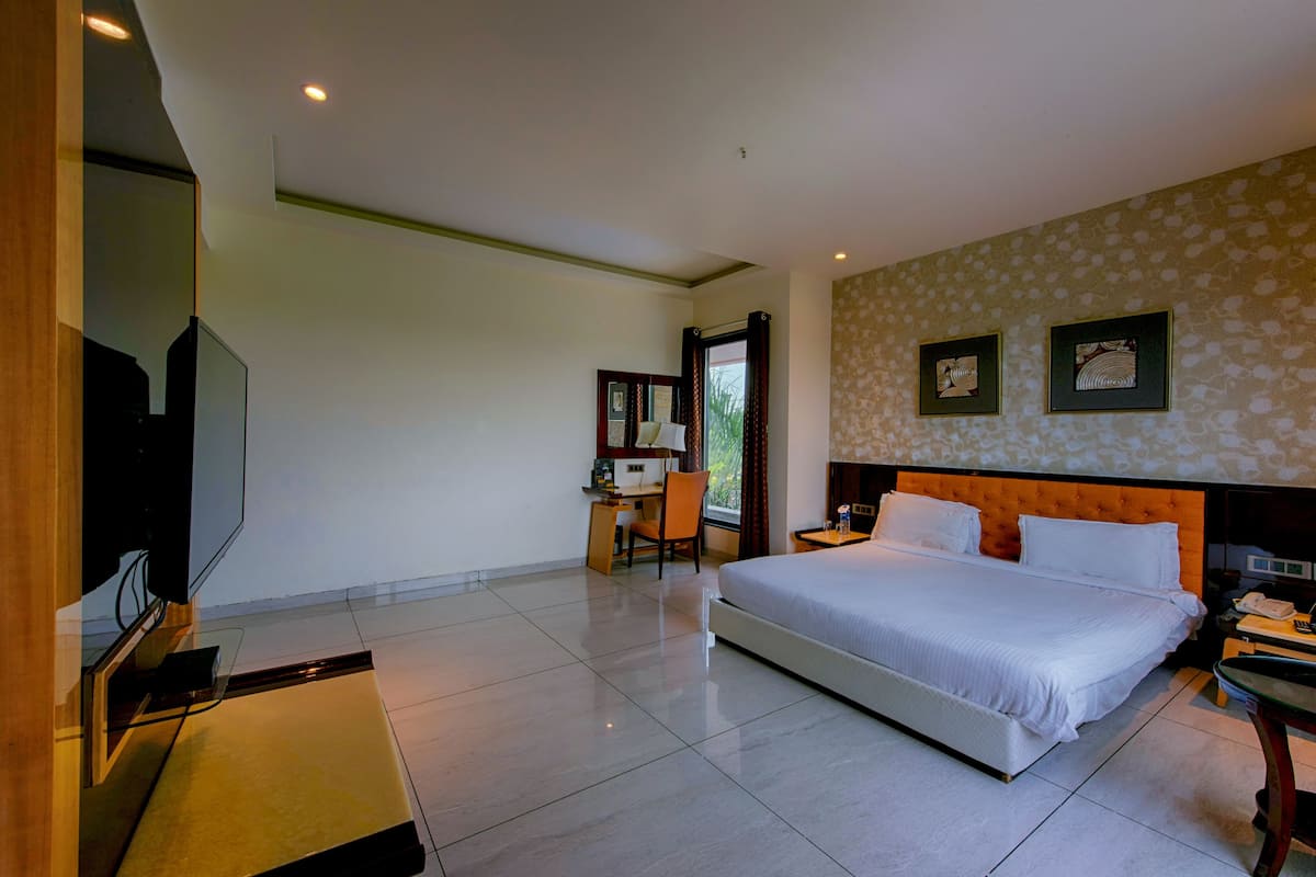 A hotel room with a large bed, a desk with a chair, a television, and two framed pictures on the wall.