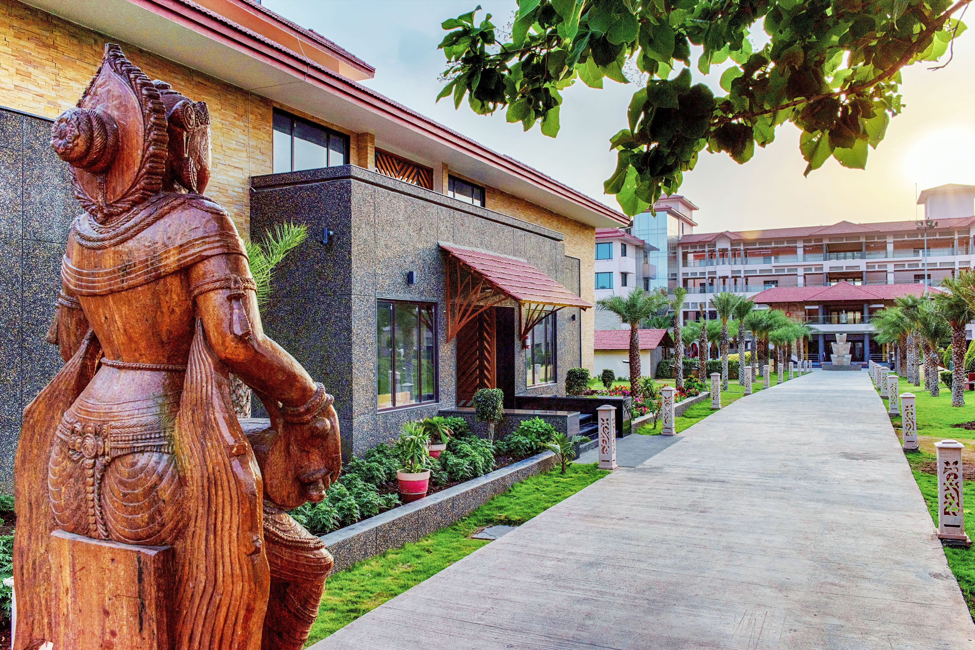 A modern building with a large wooden sculpture, a paved walkway, and a well-maintained garden.