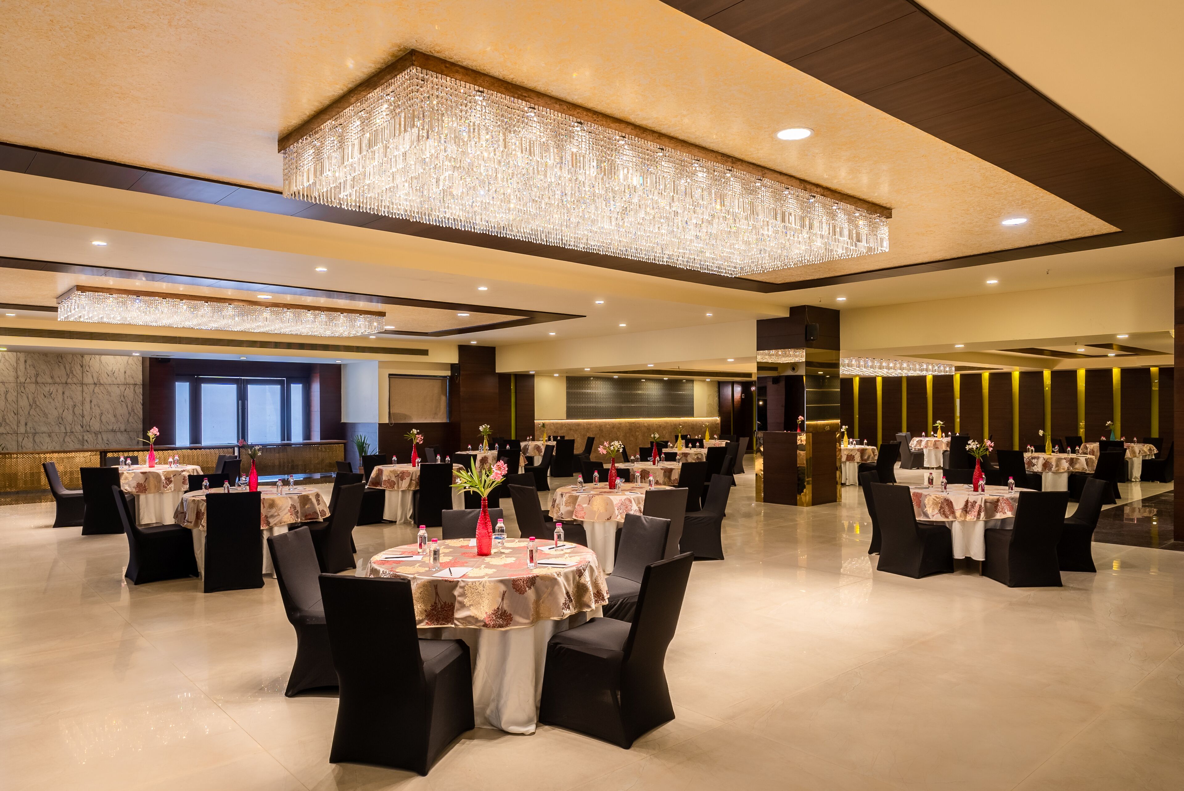 Une salle de banquet spacieuse, avec des tables rondes, des chaises noires et un grand lustre.