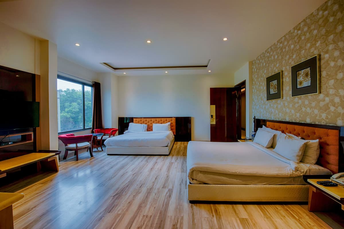 A hotel room with a large bed, a smaller bed, a desk, a TV, and a window with curtains.