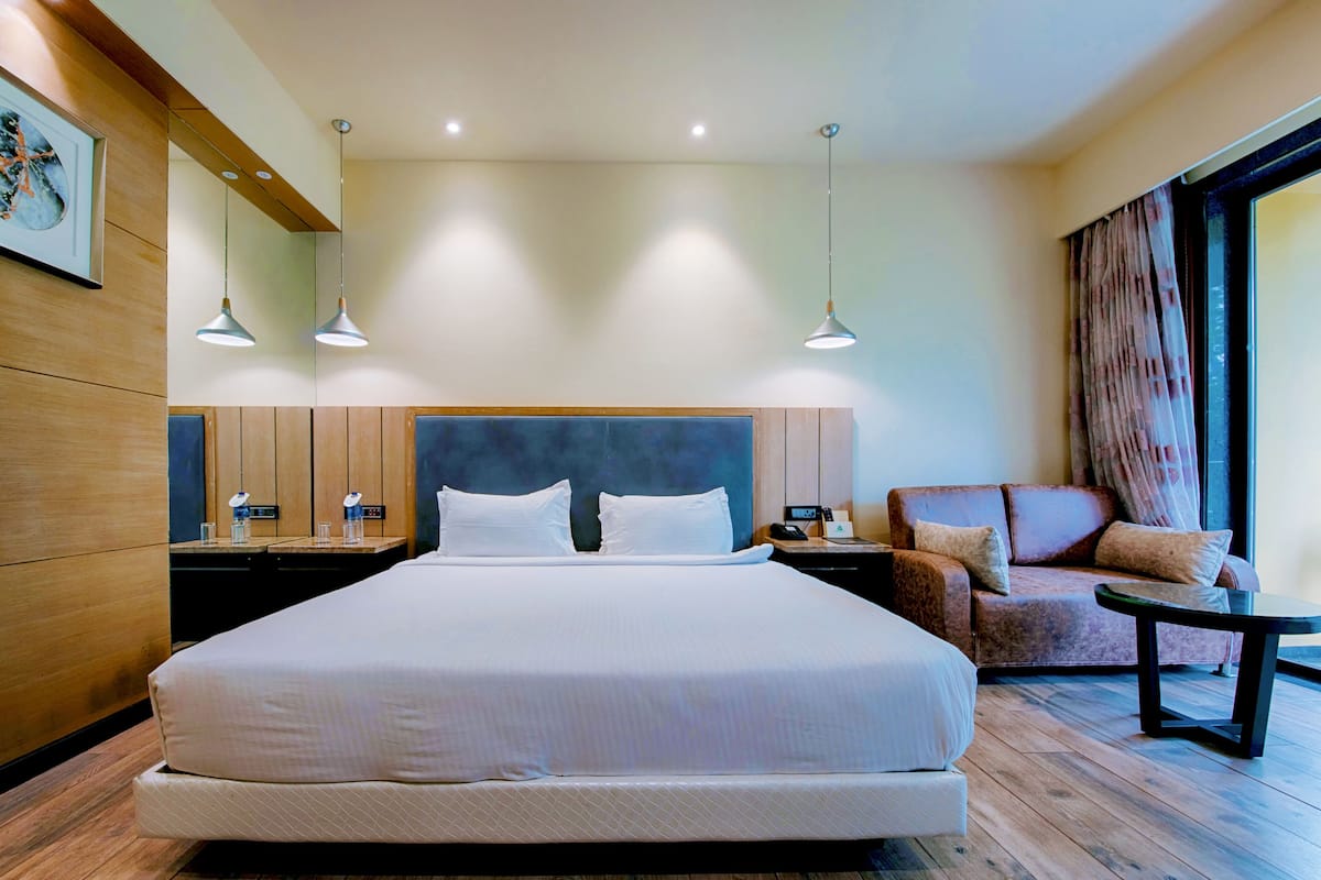 A hotel room with a large bed, bedside tables, a sofa, and a small table.