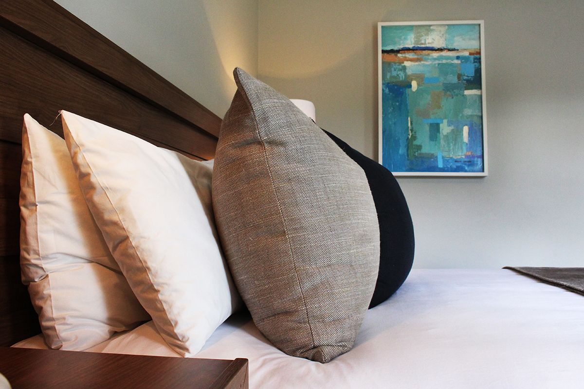 A bed with three pillows and a painting on the wall.