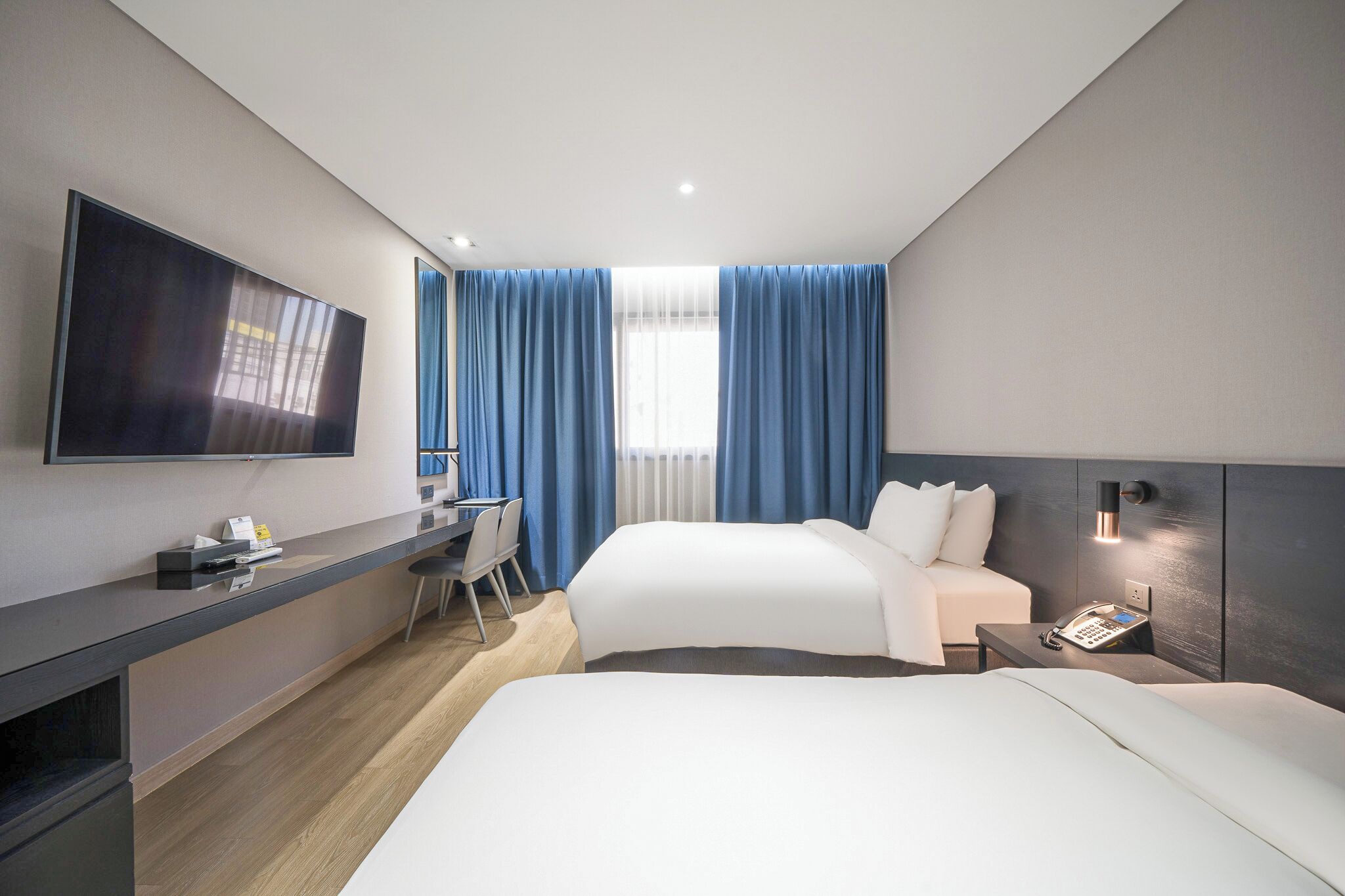 Habitación de hotel moderna con dos camas, un escritorio, un televisor de pantalla plana y una ventana con cortinas azules.