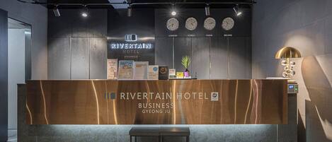 A reception desk at Rivertain Hotel with clocks displaying time in London, Korea, Paris, and Beijing.
