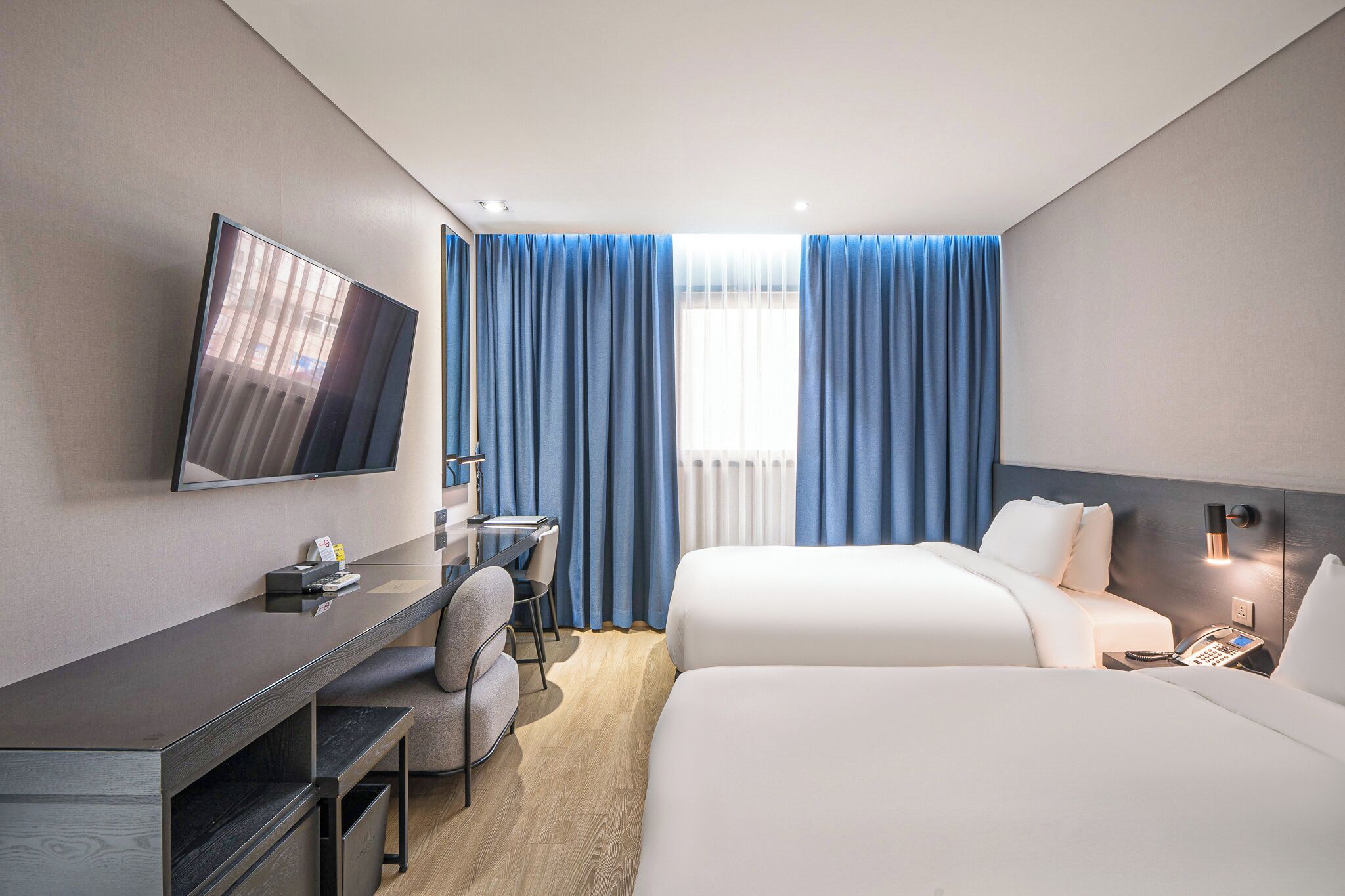 Una habitación de hotel con cama, escritorio con silla, televisor y ventana con cortinas.