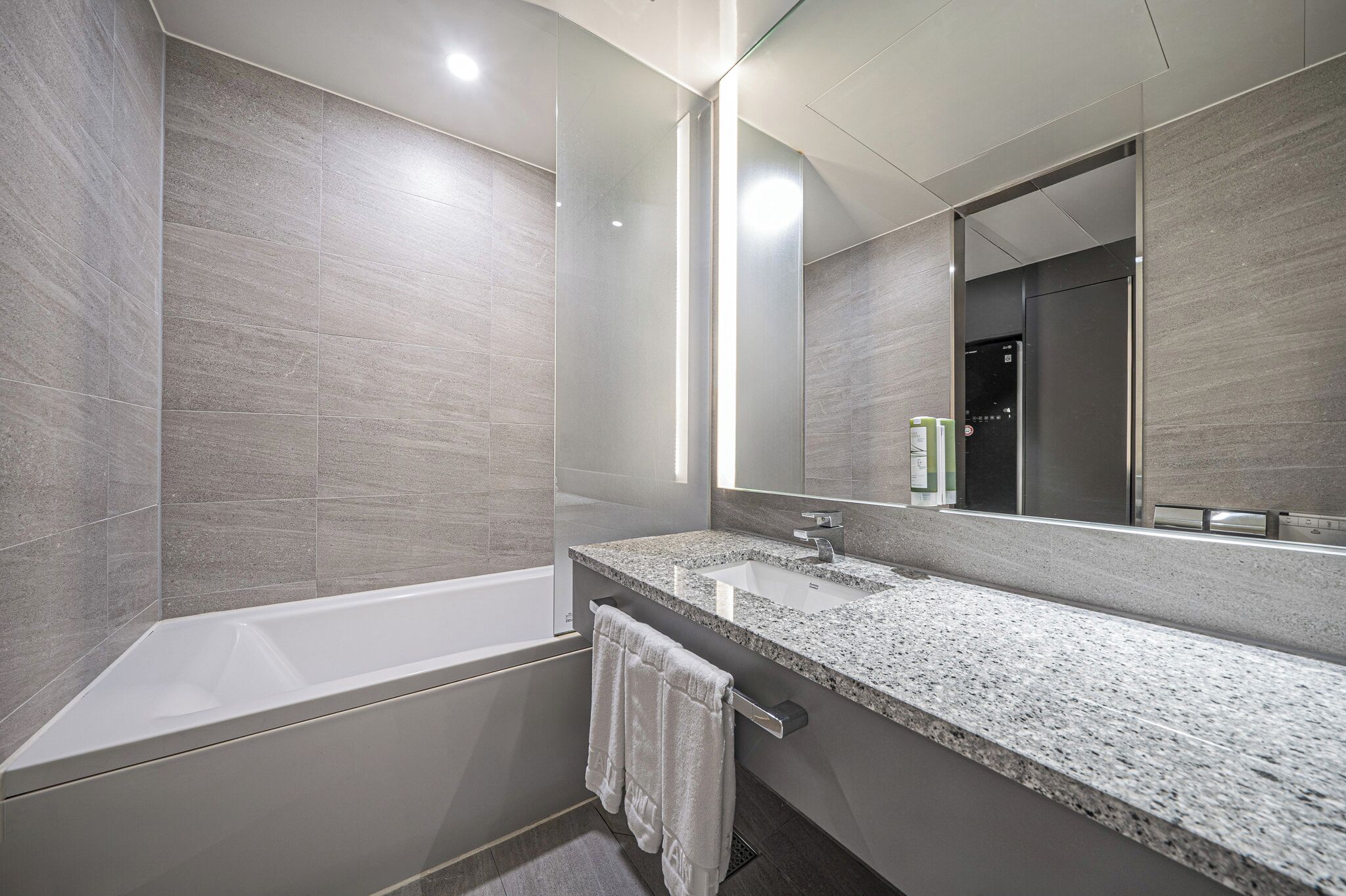 Un baño moderno con bañera, un espejo grande y encimera de granito.