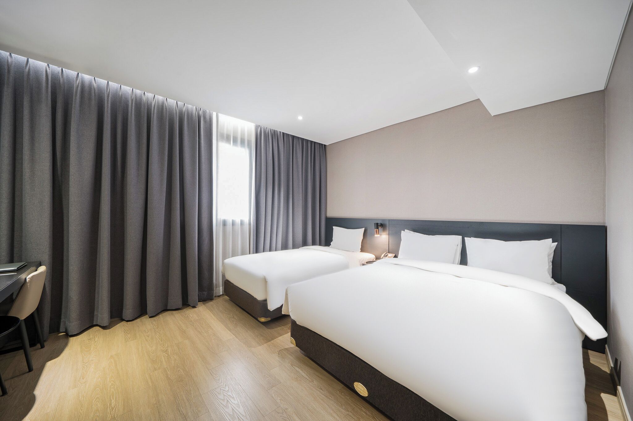A hotel room with two beds, a desk, and a chair.