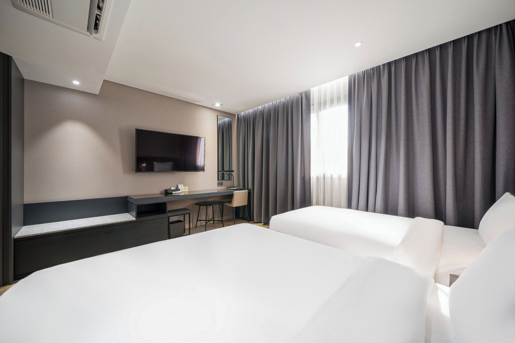 A modern hotel room with a large bed, a desk, a flat-screen TV, and a large window with curtains.