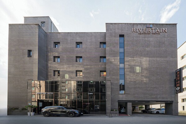Ein modernes Geschäfts-Hotel mit markantem Eingang, einem Café und einem Parkbereich.
