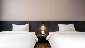 A hotel room with two beds, a bedside table with a phone, and a wall-mounted light fixture.