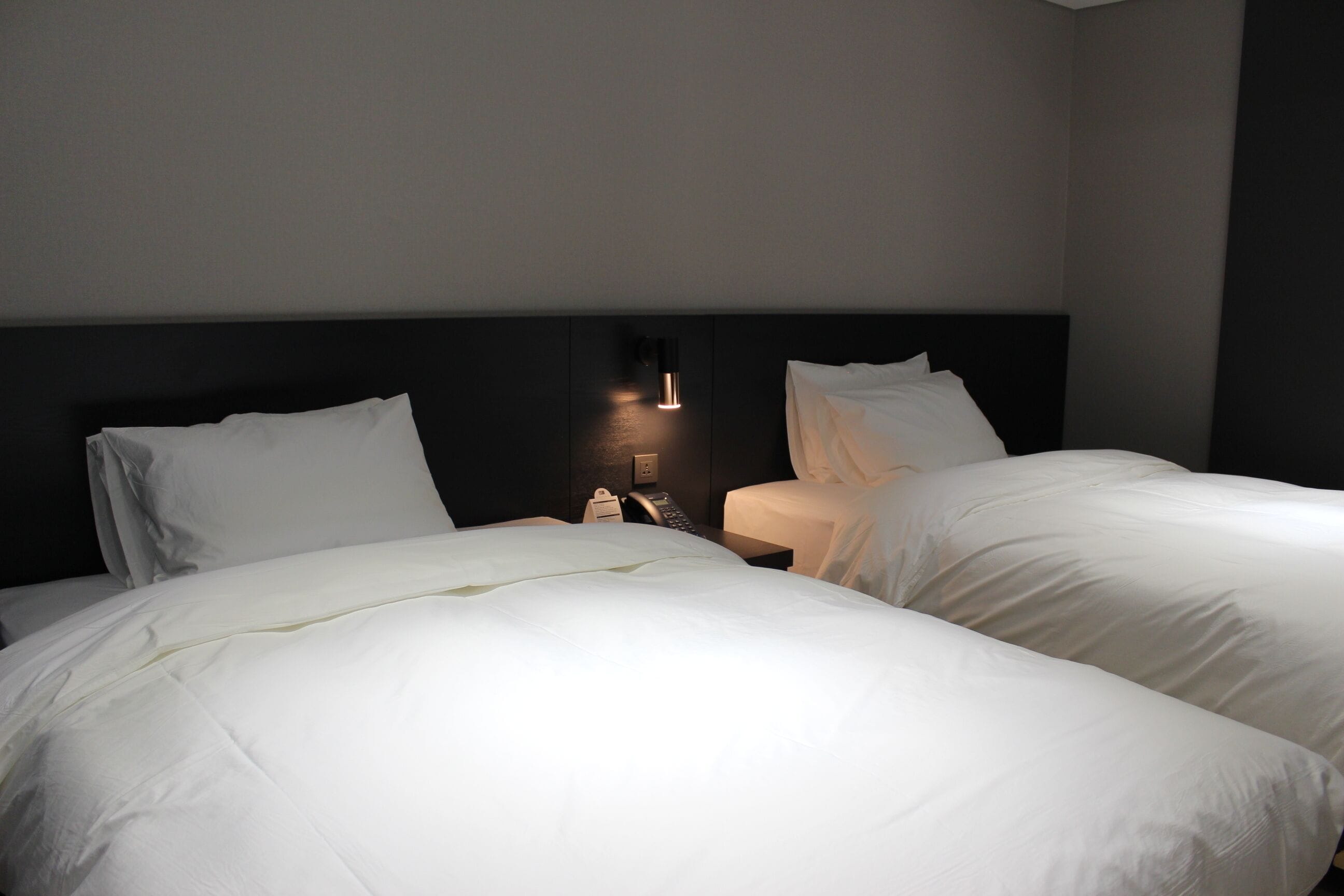 Une chambre d’hôtel avec deux lits, une table de chevet avec une lampe et un luminaire fixé au mur.