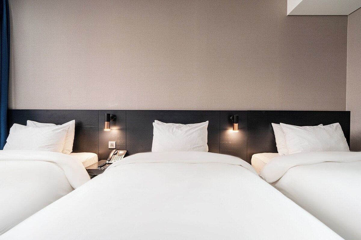 A hotel room with two beds, a nightstand, and a wall-mounted phone.