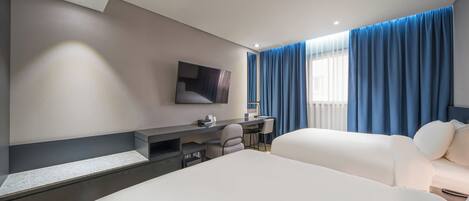 A modern hotel room with a large bed, a desk with a chair, a flat-screen TV mounted on the wall, and a window with blue curtains.