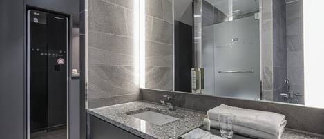A modern bathroom with a granite countertop, a large mirror, a glass shower enclosure, and a towel rack.
