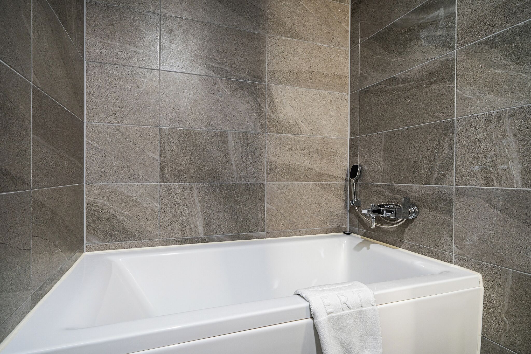 A modern bathroom with a bathtub, grey marble tiles, and a chrome faucet.