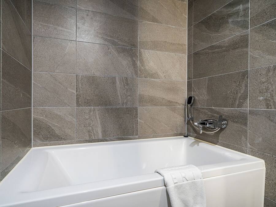 A modern bathroom with a bathtub, grey marble tiles, and a chrome faucet.