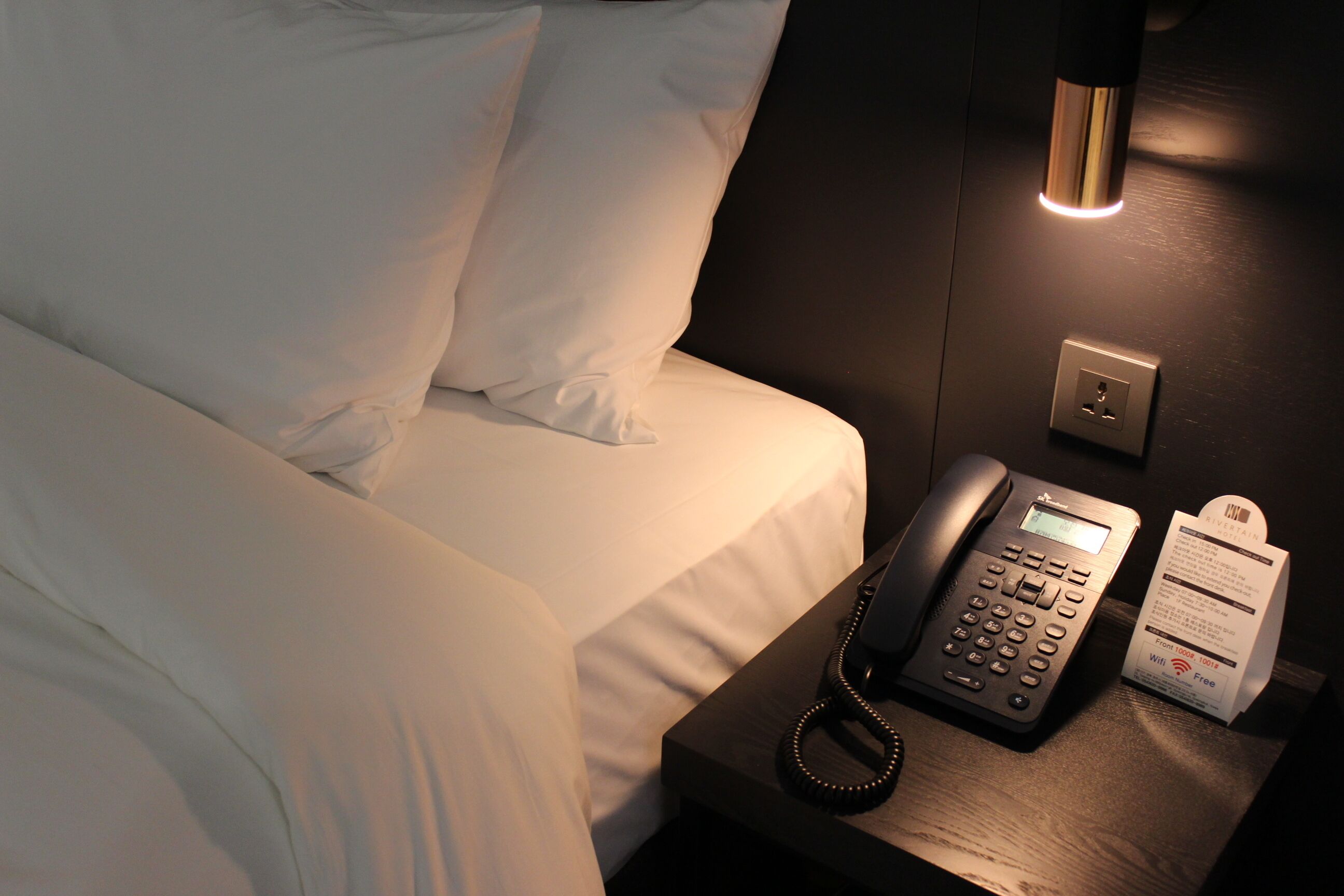 Een hotelkamer met een bed, telefoon op het nachtkastje en een lamp.