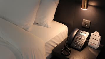 Een hotelkamer met een bed, telefoon op het nachtkastje en een lamp.