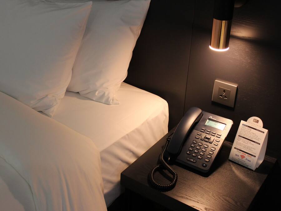 Een hotelkamer met een bed, telefoon op het nachtkastje en een lamp.